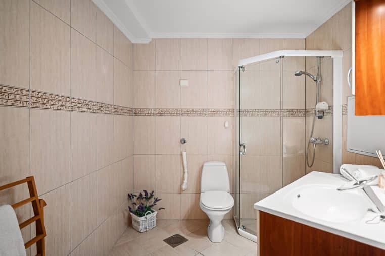 Vue d’une douche moderne encadrée de boiseries claires et de carreaux gris.