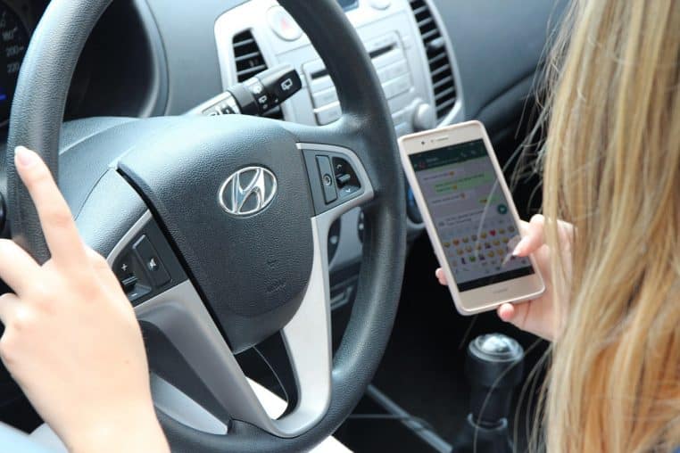 Main d’un conducteur tenant un smartphone au-dessus du tableau de bord.