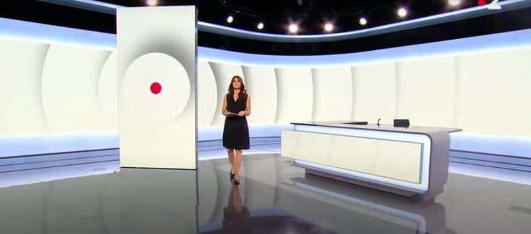 Vue large du plateau ultramoderne de France 2 ; Sonia Chironi debout en robe noire au centre, colonne vidéo à motif cercle rouge.