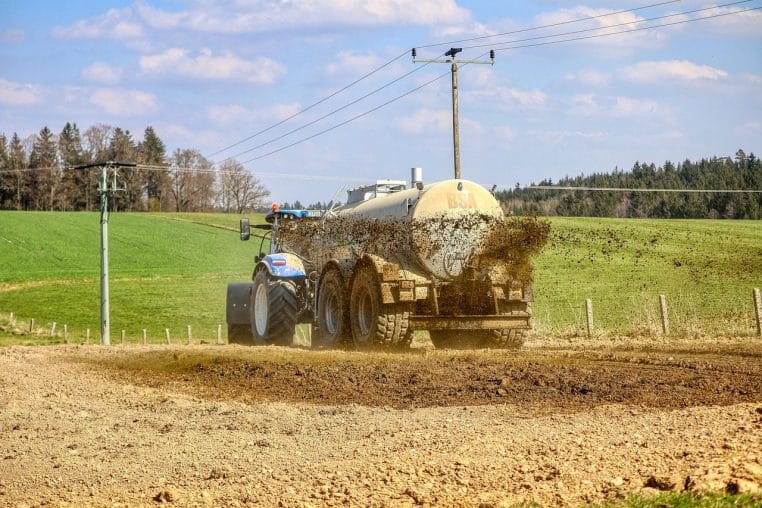 Tracteur jaune épandant du lisier dans un vaste champ vert sous un ciel nuageux.