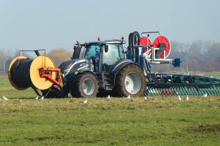 Tracteur orange épandant du fumier liquide dans une prairie herbeuse.