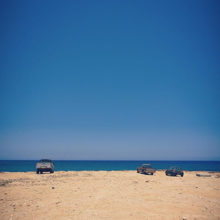 Trois voitures garées sur une plage de sable face à la mer.