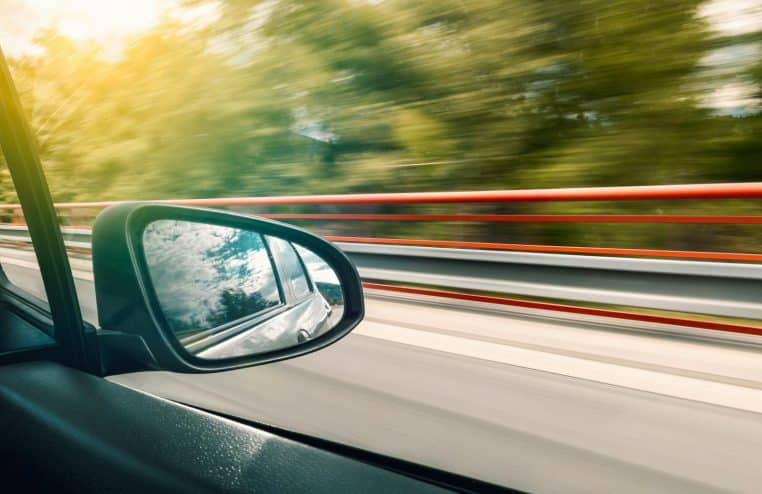 Side mirror view capturing high-speed travel on an expressway with motion blur effect.