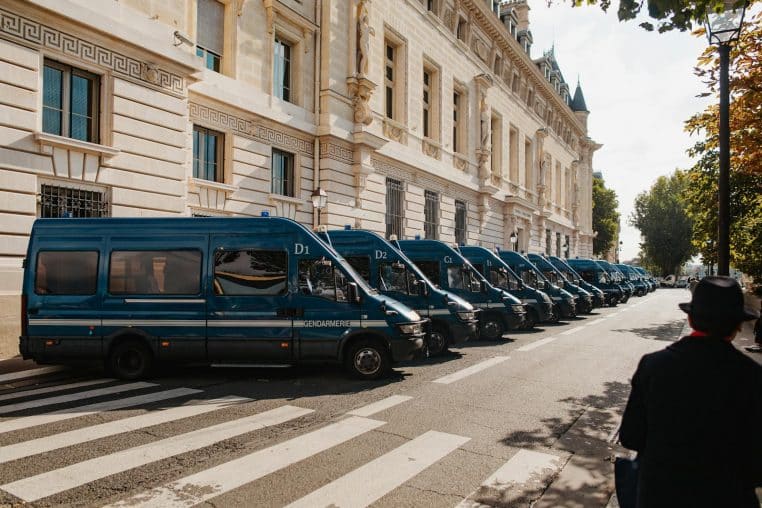 Line of blue police vans parked on a city street beside a historical building.