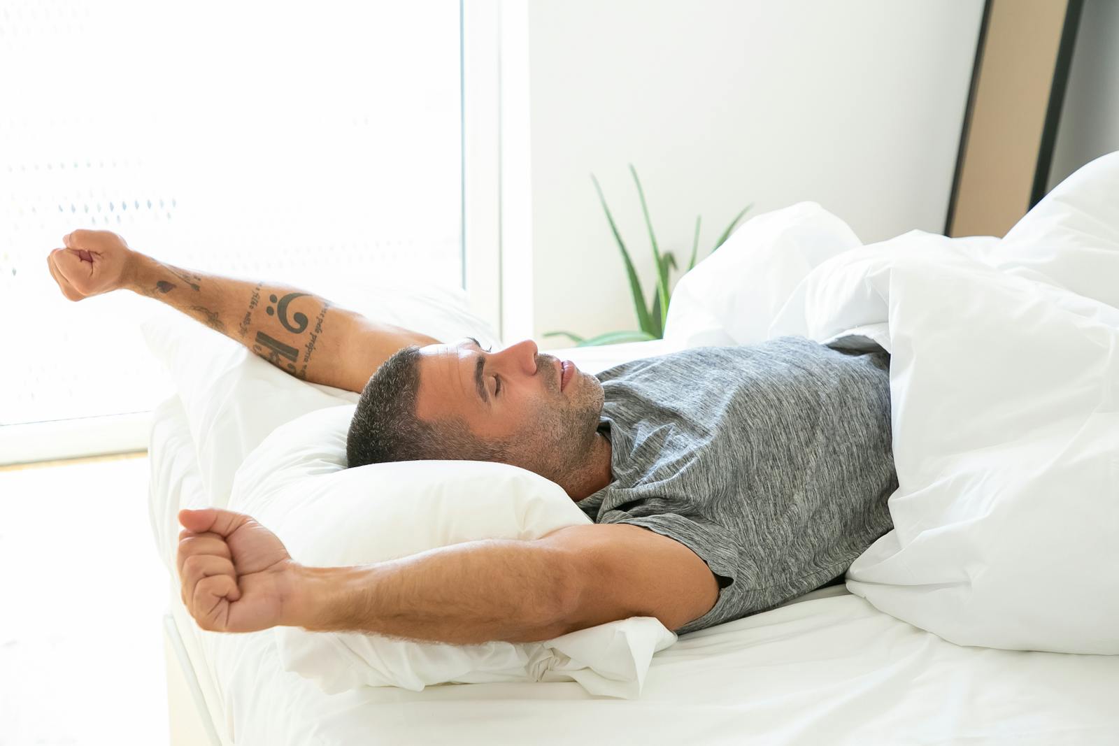 Adult man stretching in bed, looking relaxed and refreshed in the morning light.