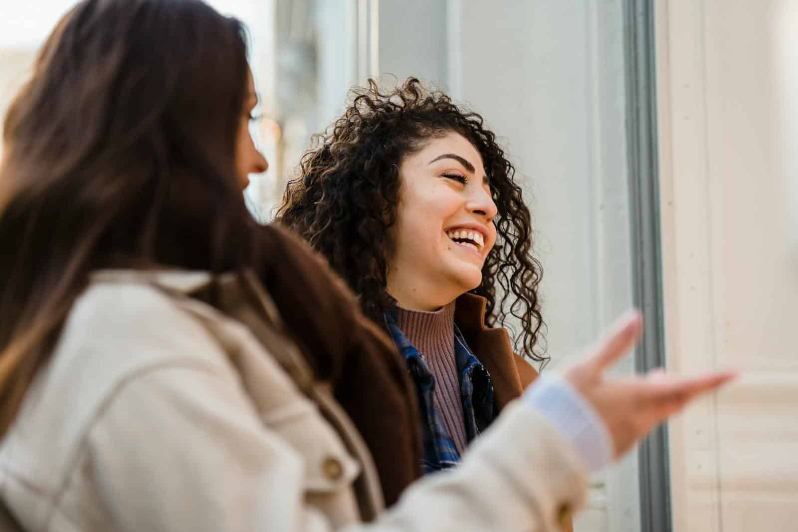 Two young women sharing a light moment and laughing on an urban street during the day.