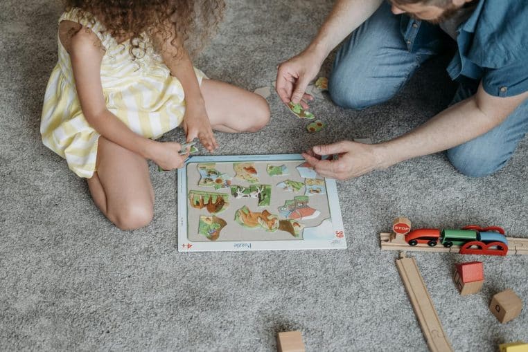A father and daughter bonding over a puzzle on the living room floor, featuring toys and a puzzle.