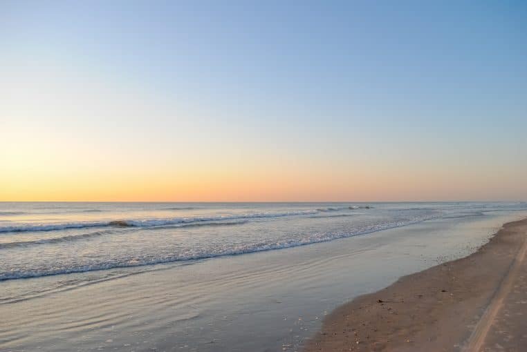 Rivage calme au lever du soleil avec petites vagues et ciel dégagé.