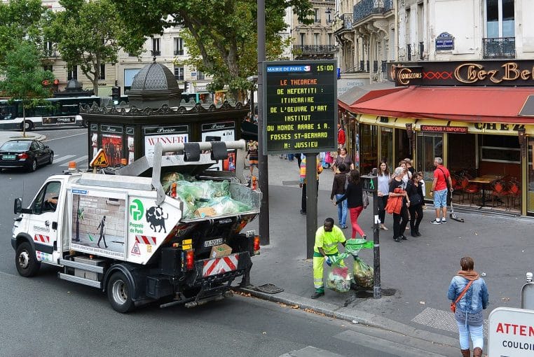 Camion de collecte des déchets à Paris, devant un kiosque à journaux.