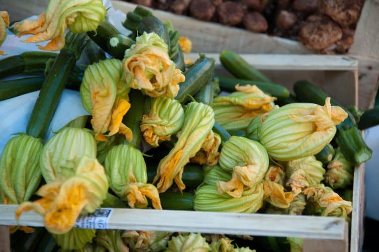 Courgettes et fleurs de courgette disposées sur un étal de marché.