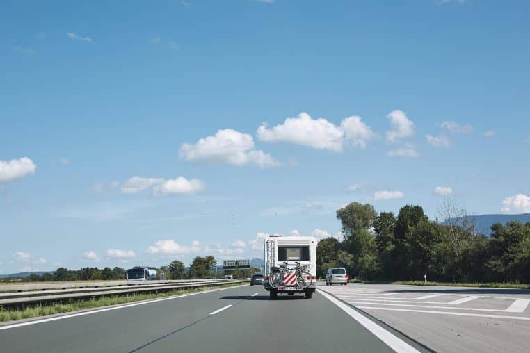 Caravane blanche tractée sur l’autoroute en été, vue arrière.