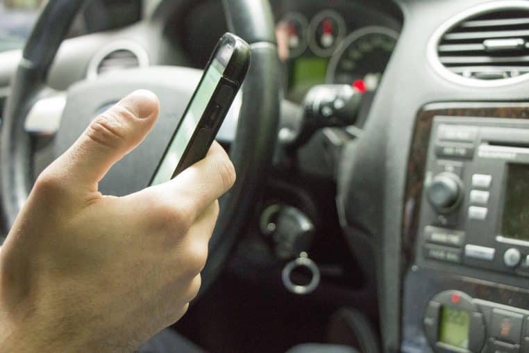 Conducteur tenant un smartphone au-dessus du volant dans l’habitacle d’une voiture
