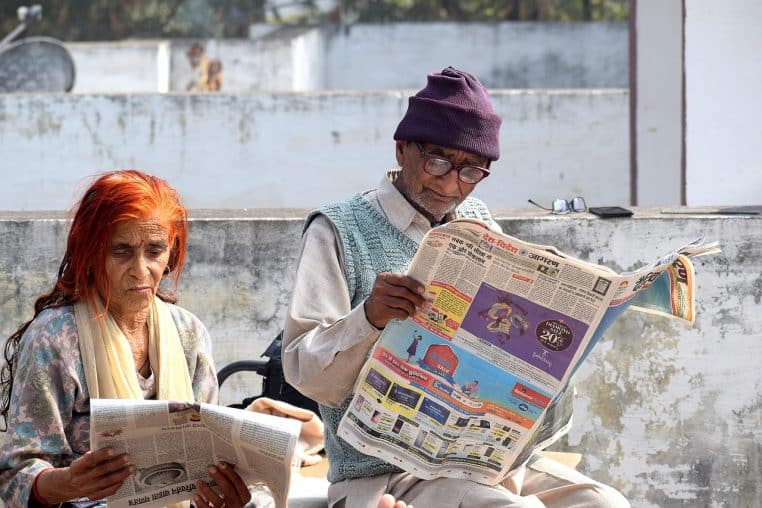 Deux personnes âgées assises sur un banc, lisant un journal.
