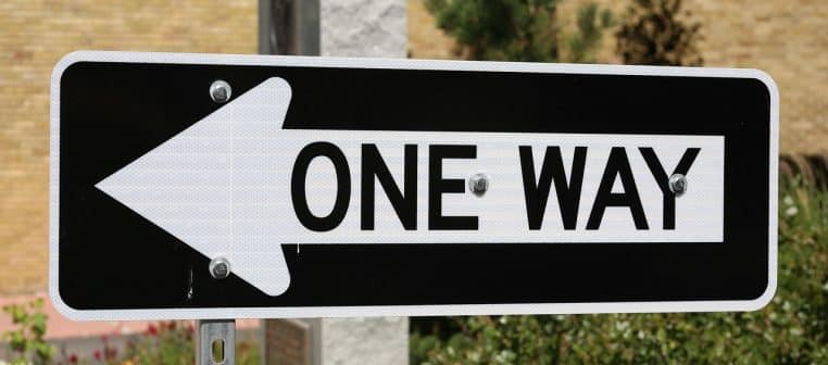 Gros plan d’un panneau « One Way » avec flèche, monté sur un poteau métallique en ville.