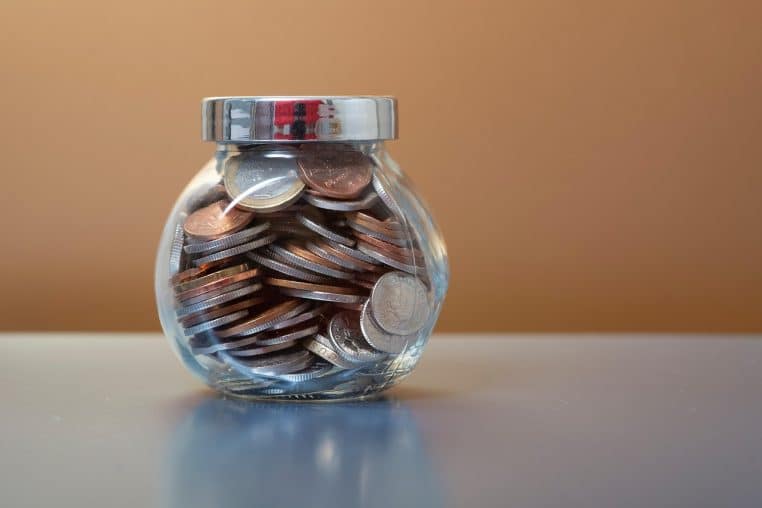 Pot en verre transparent rempli de pièces brillantes posé sur une table en bois.