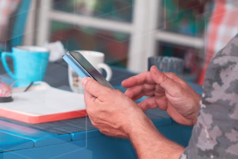 main tapant un SMS à un doigt près d’une tasse de café.