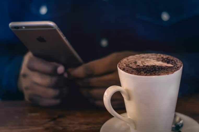 Un individu utilise son smartphone avec son café à coté.