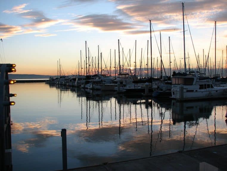 Pier et navires au petit matin avec ciel orangé et brume légère.