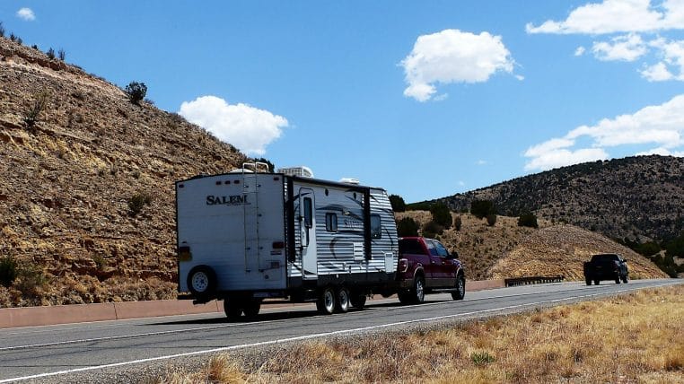 Voiture tractant une caravane sur route dégagée, ciel bleu.
