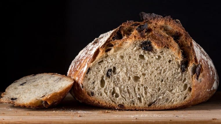 Delicious artisan olive bread loaf with one slice on wooden board, perfect for healthy eating.