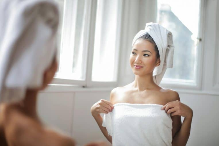 Young woman enjoying a cozy bath moment with a towel in a bright bathroom, reflecting happiness.