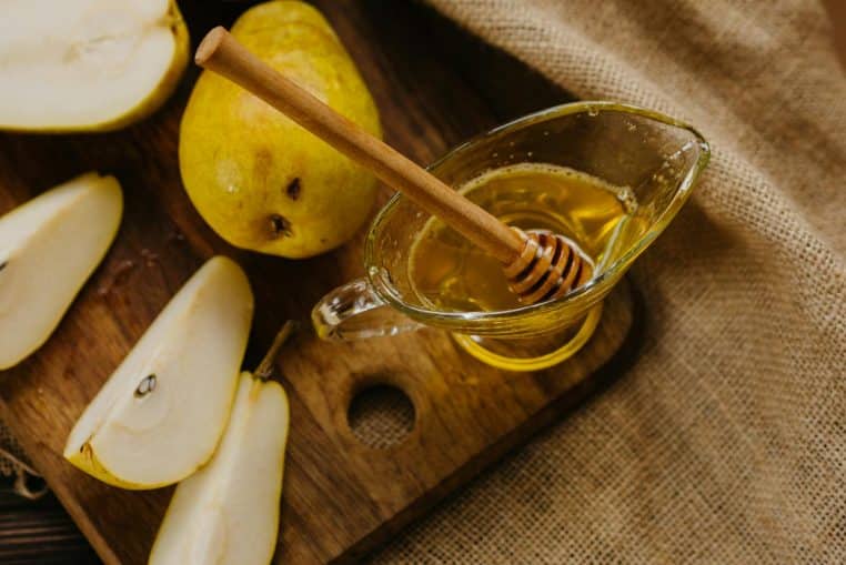 A rustic still life of sliced pears with honey drizzler on a wooden cutting board.