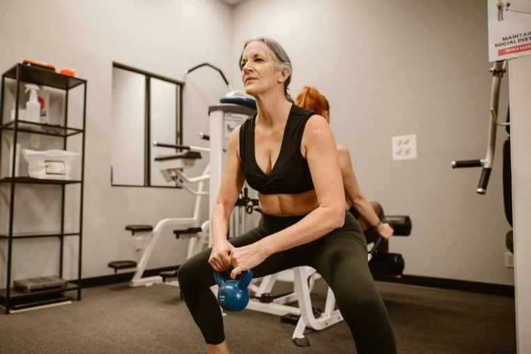 Active senior woman performing kettlebell squats for strength training at indoor gym.