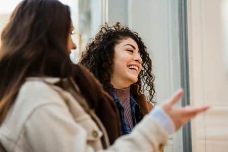 Two young women sharing a light moment and laughing on an urban street during the day.