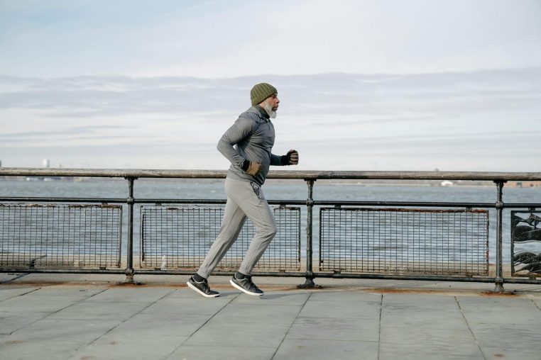 Elderly man running along waterfront, embracing a healthy lifestyle and exercise routine.