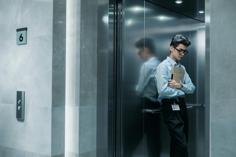 Young man in an elevator holding papers, deep in thought.
