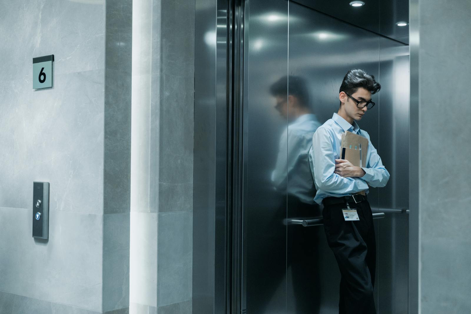 Young man in an elevator holding papers, deep in thought.