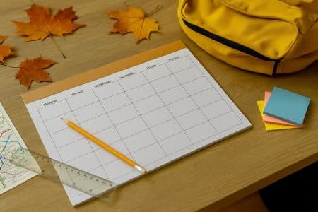 Planificateur mensuel posé sur un bureau en bois avec crayon, règle et feuilles d’érable — ambiance rentrée 2025-2026.