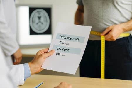 Médecin examinant des résultats de triglycérides et de glucose aux côtés d’un tour de taille mesuré, avec une imagerie cérébrale floutée en arrière-plan.