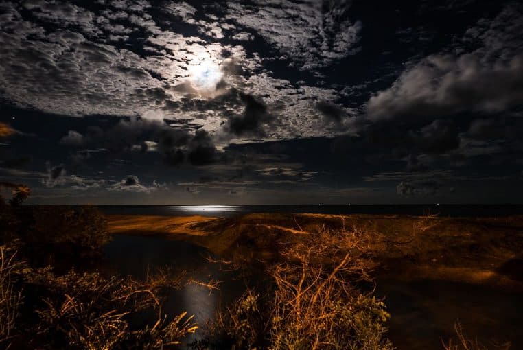 Lune pleine se reflétant sur l’océan, ciel sombre et horizon dégagé.
