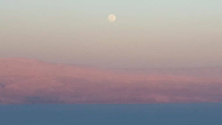 Lune pleine haute dans le ciel au-dessus d’une étendue d’eau calme.