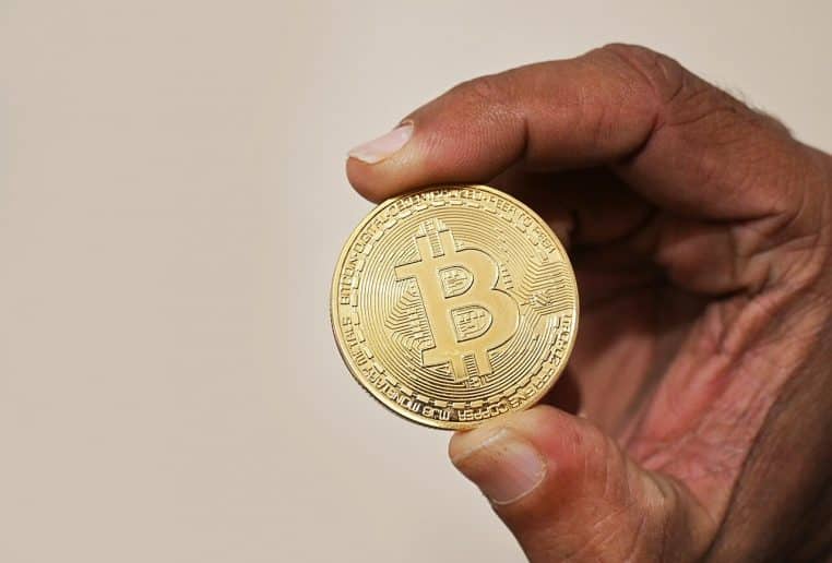 Gros plan d’une pièce bitcoin tenue entre deux doigts.