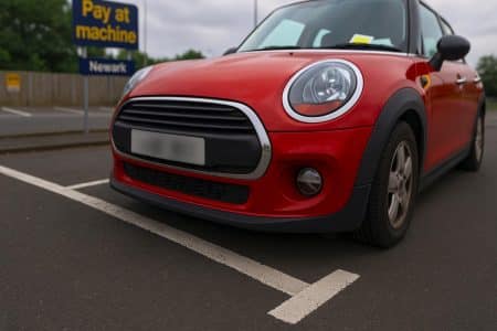 Mini rouge garée sur un parking payant à Newark, roue avant mordant légèrement sur la ligne blanche.