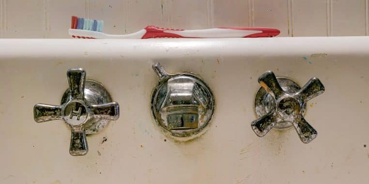 Brosse à dents posée sur le bord d’un évier ancien.