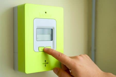 Main appuyant sur le bouton « + » d’un compteur Linky pour afficher la puissance souscrite, gros plan en lumière naturelle, fond légèrement flou.