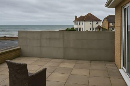 Mur en béton bloquant la vue sur la mer depuis une terrasse à Poole, maisons côtières au second plan, ciel couvert.