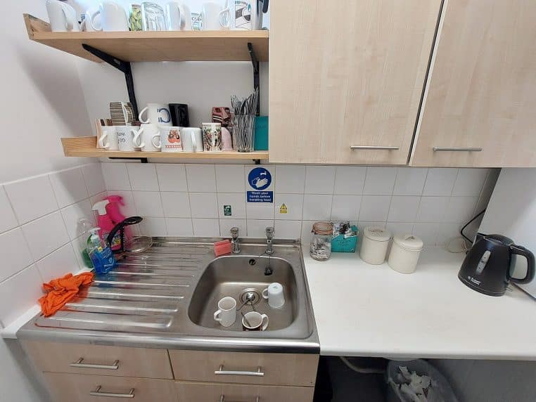 Petite cuisine équipée avec évier, bouilloire et mugs posés.