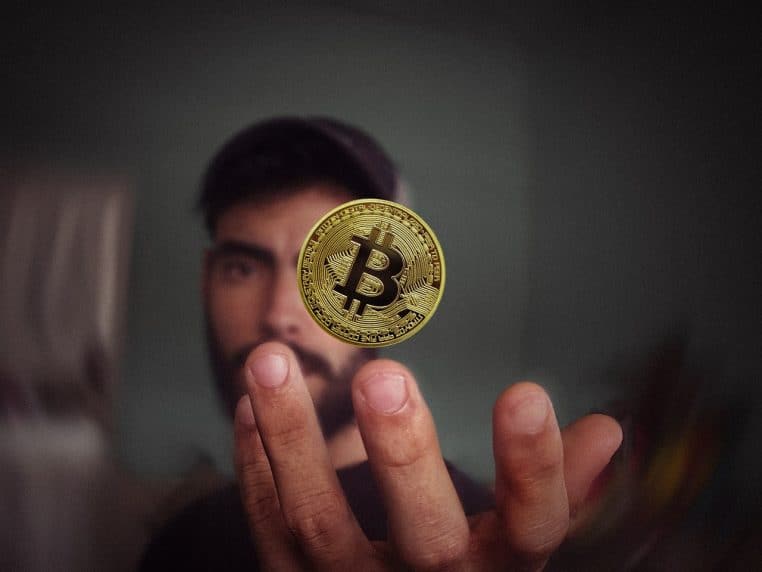 Main tenant une pièce bitcoin dorée.