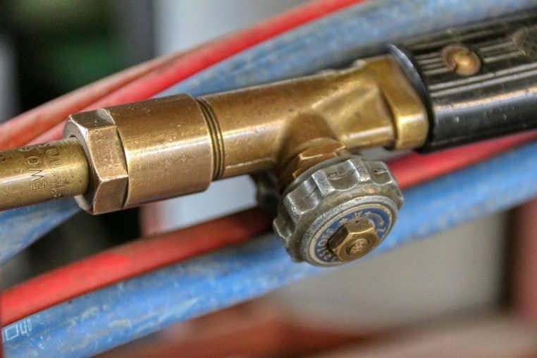 Gros plan sur le robinet et la tête d’un chalumeau oxyacétylénique, relié à des tuyaux rouge et bleu.