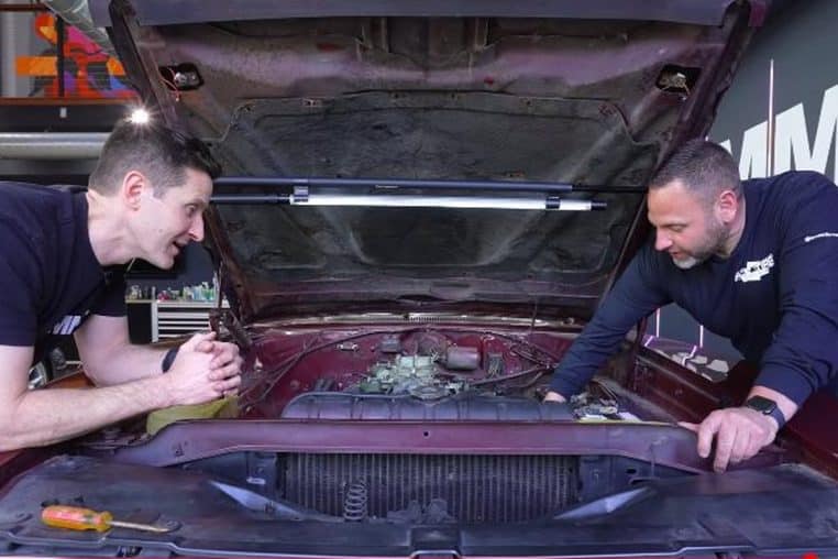 Inspection du V8 sous capot ouvert d’une Dodge Charger 1968 chez AMMO NYC, deux techniciens à l’ouvrage, outillage visible.