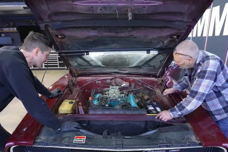 Pete et un technicien devant le V8 440 d’une Dodge Charger 1968, capot relevé, autocollant Holley sur la traverse.