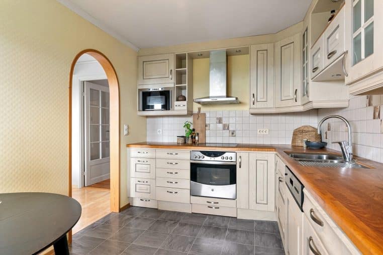 Cuisine contemporaine bois et noir, plan de travail épuré et éclairage suspendu dans un appartement moderne.