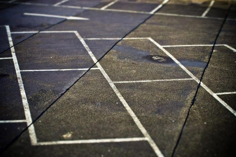 Marquage blanc d’une place de parking sur bitume, vue en plongée.