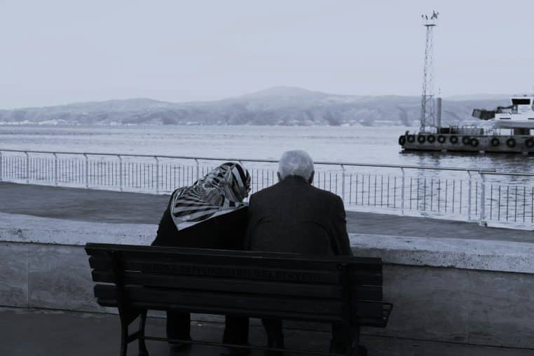 two people sitting on a bench looking out at the water