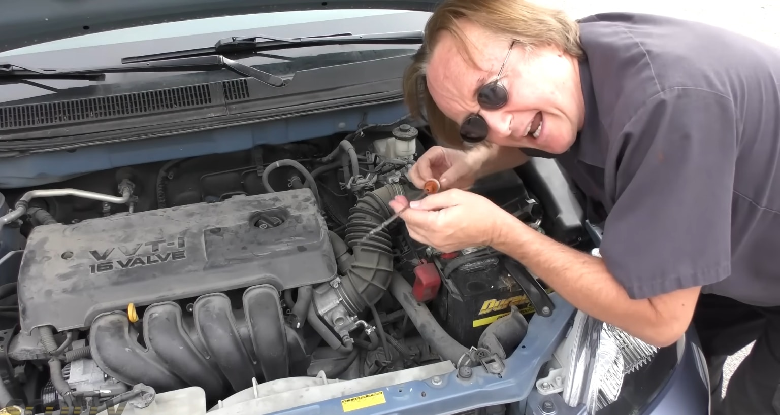 Scotty Kilmer, devant le moteur capot ouvert, vérifie la jauge d’huile d’une citadine pour illustrer les contrôles simples à faire soi-même avant d’accepter des réparations en garage.