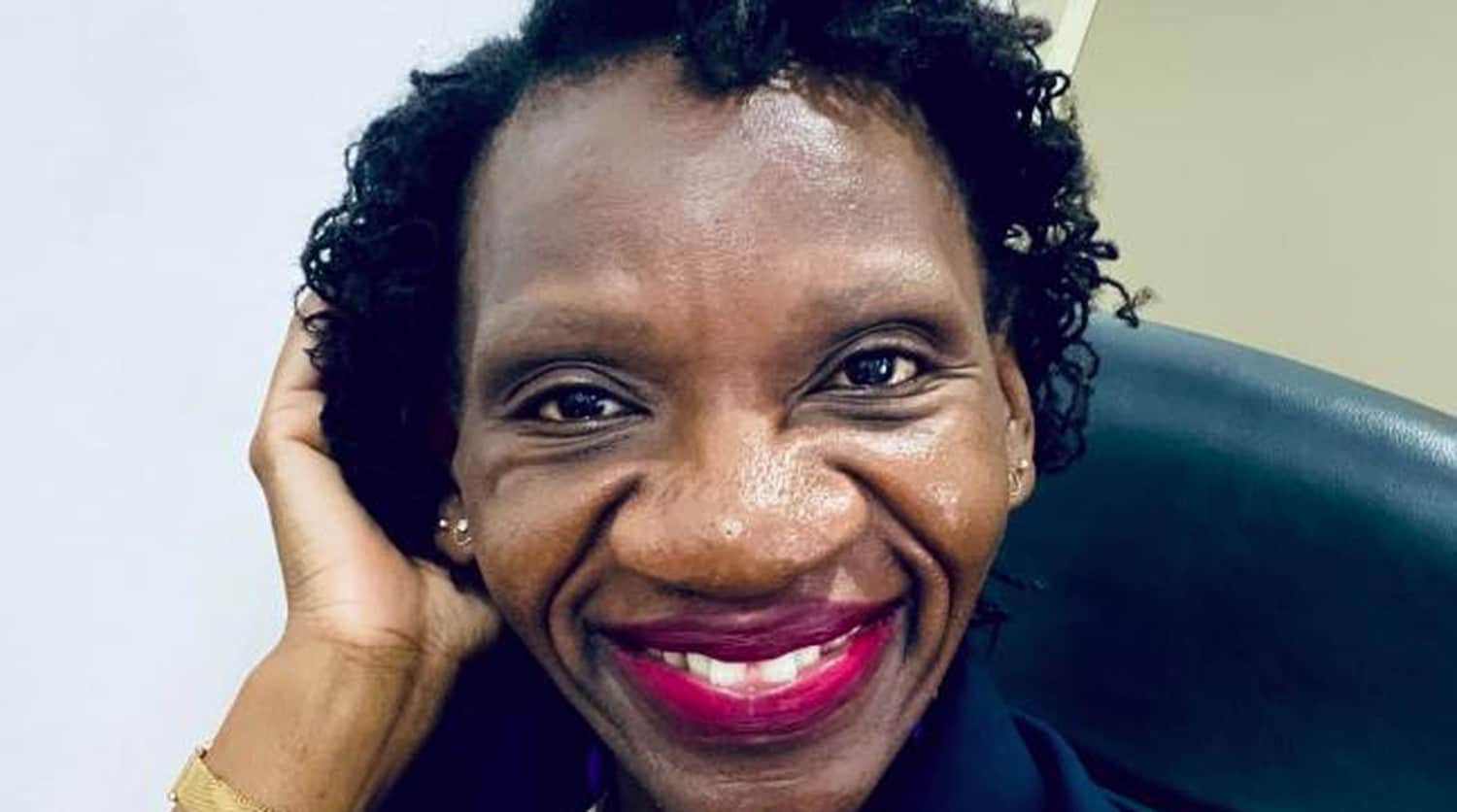 Portrait souriant d’une femme prenant un selfie au bureau, main dans les cheveux, rouge à lèvres vif.